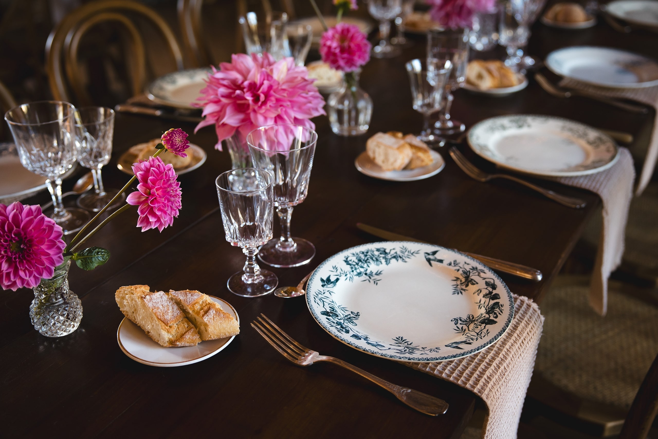 Table élégante avec dahlias roses, vaisselle ancienne à motifs bleus et verres en cristal pour un dîner raffiné.