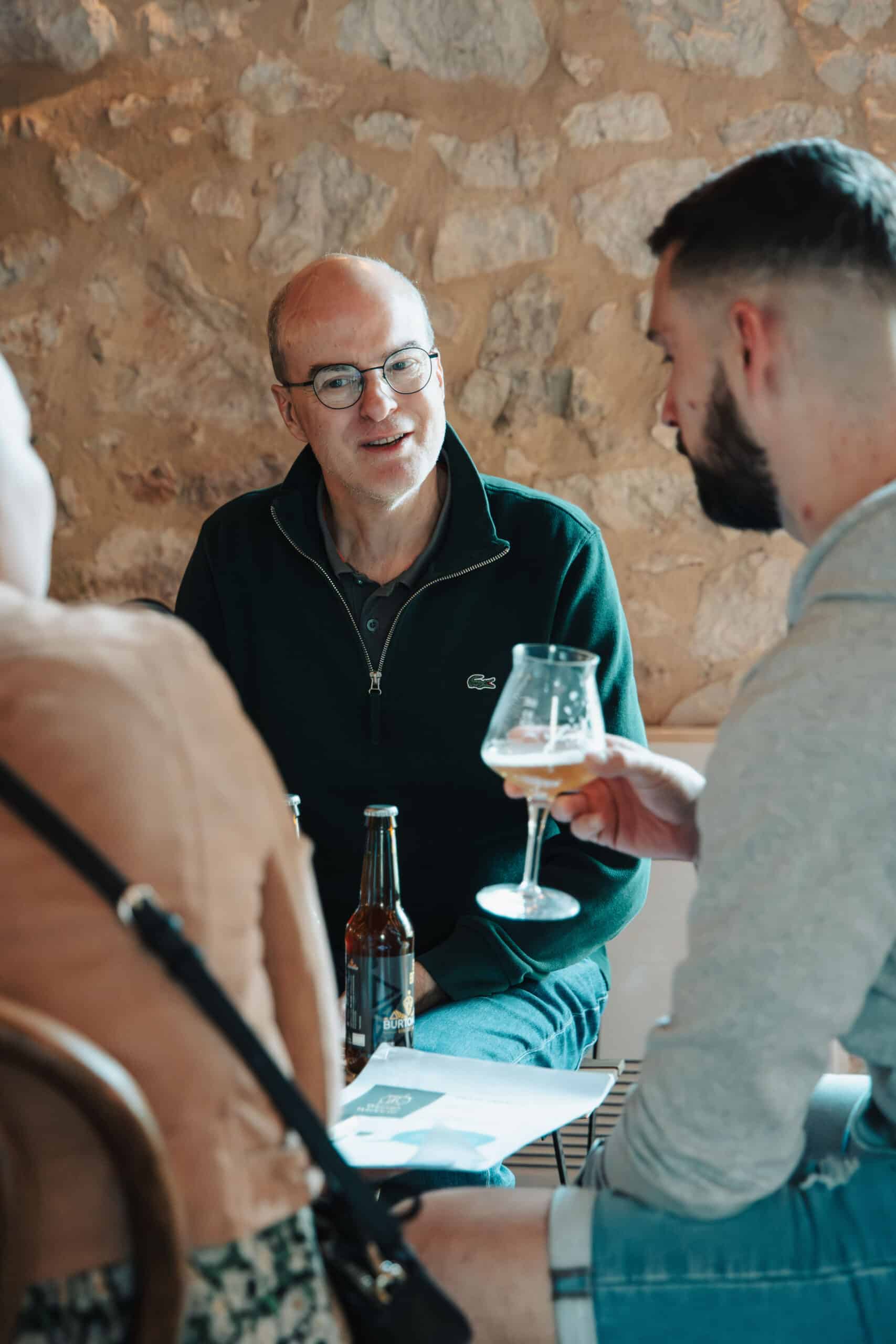Trois personnes discutent joyeusement autour d'une bière Burton dans un décor authentique en pierre.