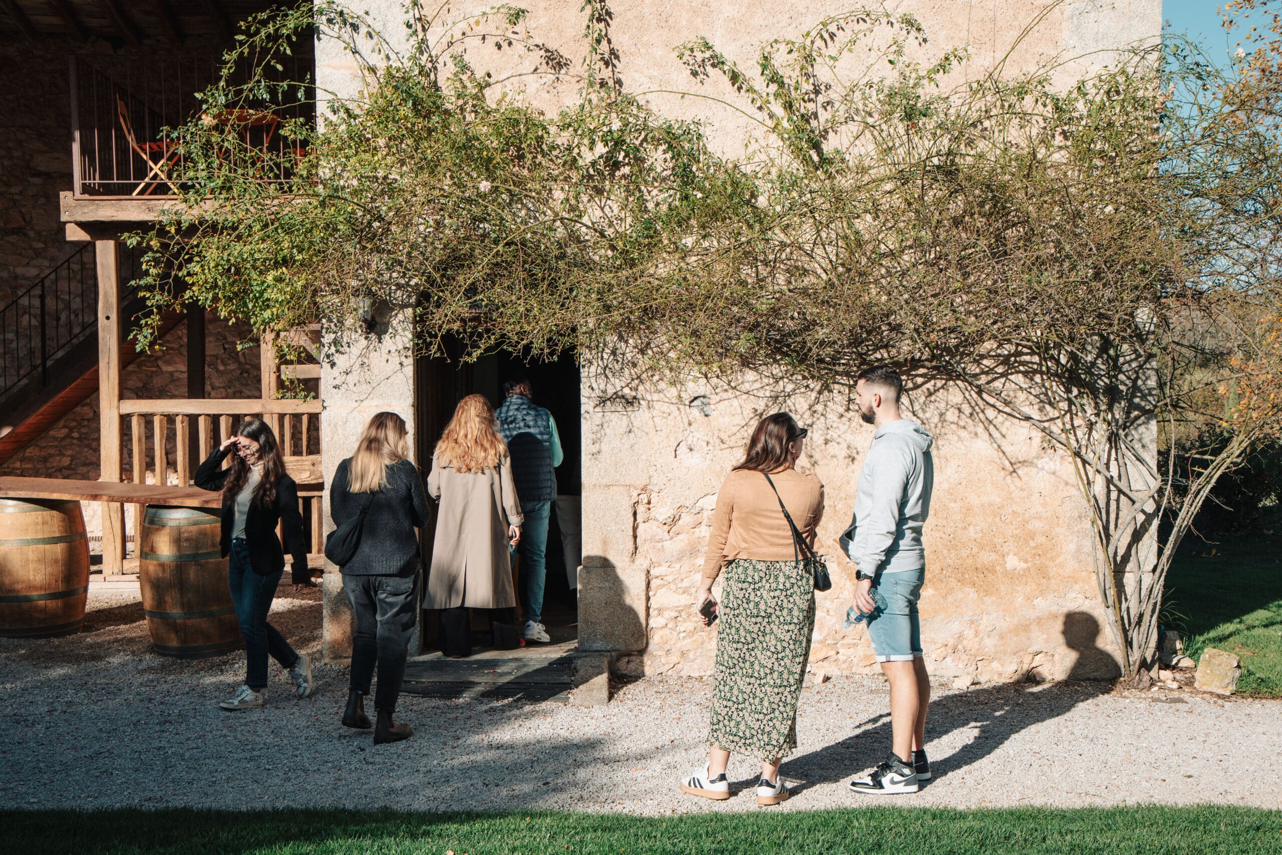 Groupe devant l'entrée du gîte Le Verger, bâtiment en pierre avec vigne grimpante et barriques en bois.