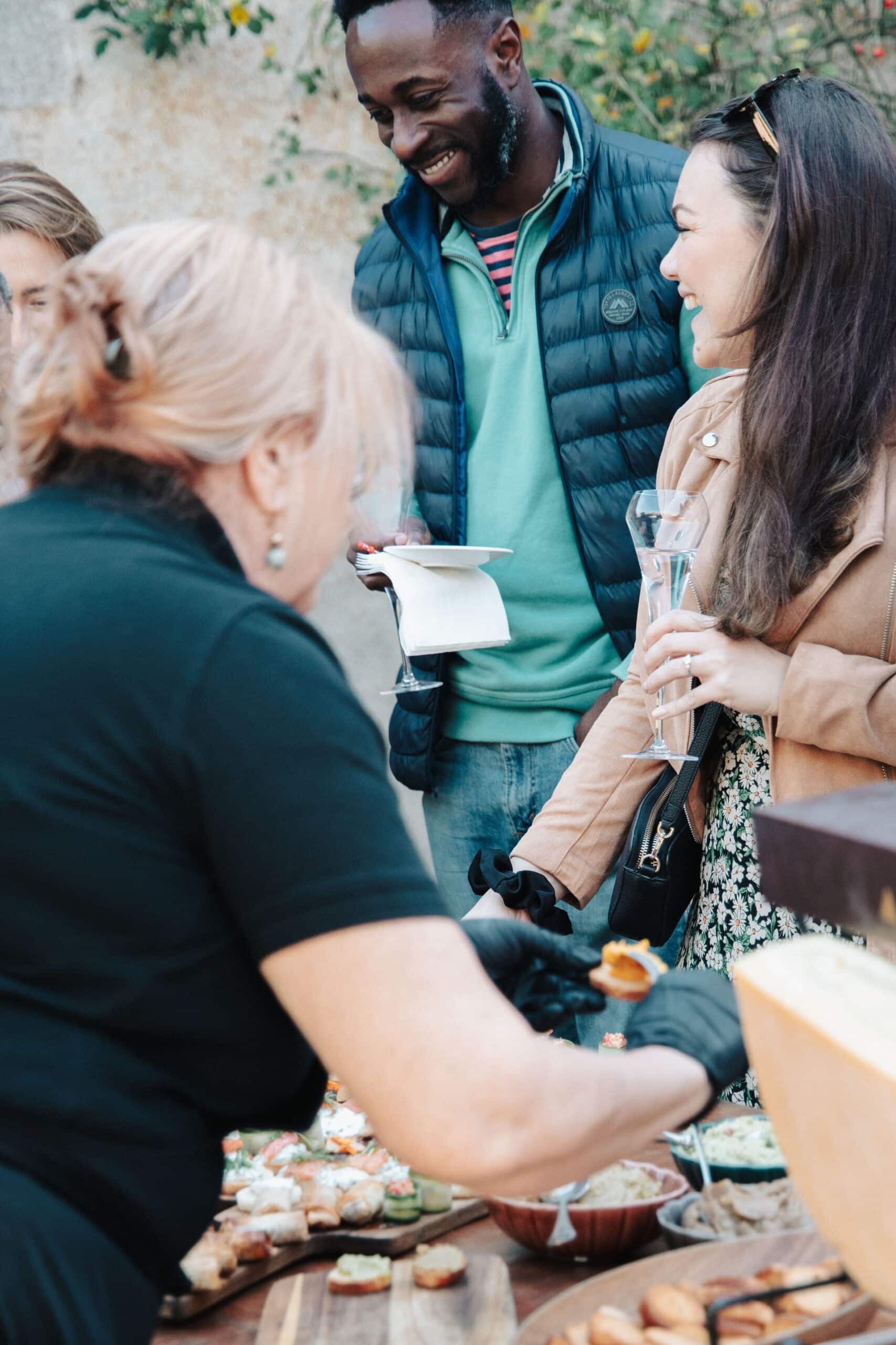 Traiteur servant des canapés à des invités souriants lors d'une réception cocktail festive en extérieur.